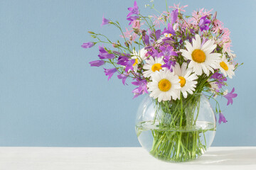 Bouquet of wildflowers in a round glass vase on a blue background

