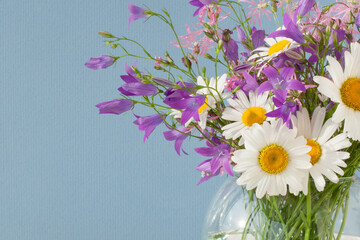 Bouquet of wildflowers in a round glass vase on a blue background
