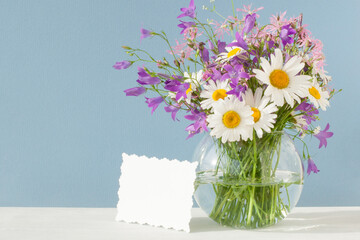 Bouquet of wild flowers in a glass round vase with a card