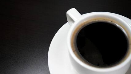 Fototapeta premium Black coffee drink. A white cup of black coffee on plate on dark table background. Morning coffee. Business table flat lay concept with coffee. Copy space.