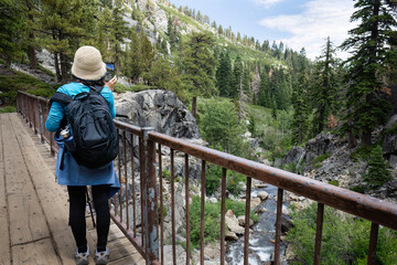 Woman taking photos using smartphone on the bridge. Eagle Lake trail. South Lake Tahoe. California.