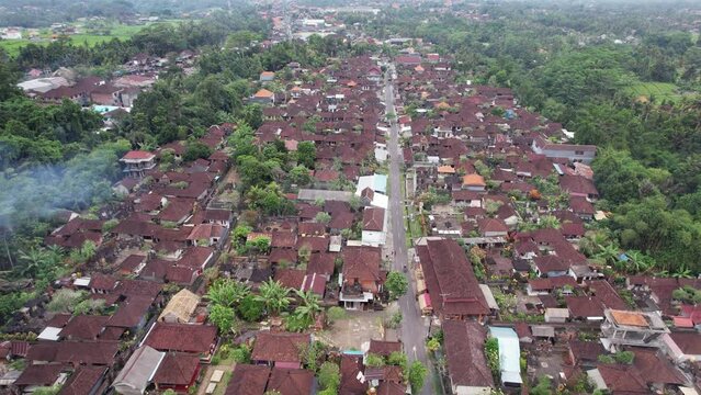 Drone view on Bali village, many traditional house compounds along narrow and straight central street. Typical elongated layout of settlement, squeezed between green forested ravines with rivers.
