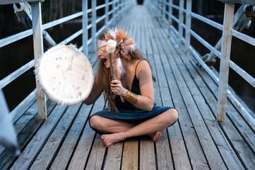 Funny shaman female playing  shamanic drum on wooden bridge, face expression