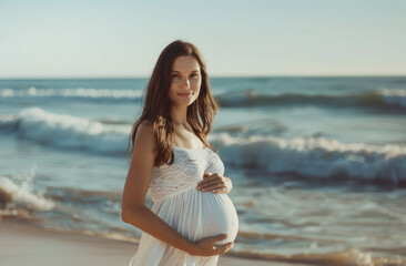 Fototapeta na wymiar A pregnant woman stands on the beach, wearing white and holding her belly with both hands.