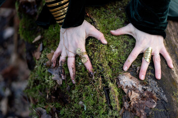 Close-up of female hands with golden rings and bracelet on green forest moss