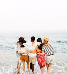 Rear view of young friends hugging each other in front of the sea on summer vacation. Holiday...