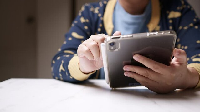 Holding a mobile tablet with one hand and browsing the internet with the other hand, an individual is checking for some updates on the newsfeed.
