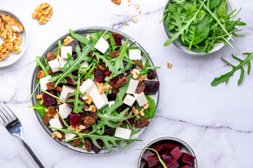 Beetroot and white cheese salad with arugula, lettuce, chard and walnuts, white table, copy space. Fresh useful vegetarian dish for healthy eating