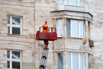 Worker in hydraulic lifting ramp washing the residential building wall
