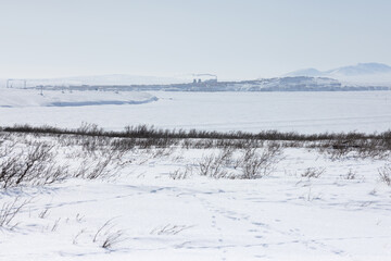 Arctic landscape. View of the snow-covered tundra and the frozen wide river. In the distance is the city of Anadyr, Chukotka Autonomous Okrug, Far North of Russia. Cold winter weather.