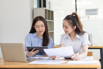 Two young asian business workers using touchpad reading document working at office.