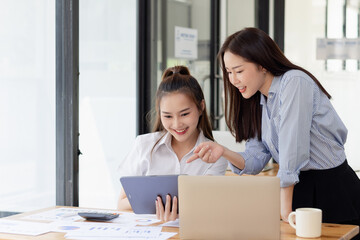 Two young asian business workers using touchpad reading document working at office.