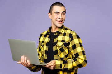 Young IT middle eastern man wear yellow shirt casual clothes hold use work on laptop pc computer look aside on area isolated on plain pastel light purple background studio portrait. Lifestyle concept.