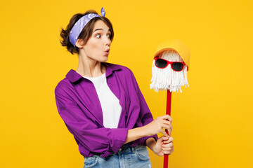 Young shocked woman wears purple shirt casual clothes do housework tidy up hold in hand mop look at...