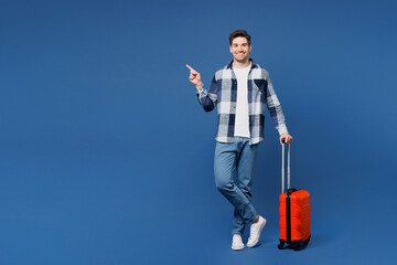 Traveler man wears shirt casual clothes hold suitcase bag point finger aside isolated on plain blue background. Tourist travel abroad in free spare time rest getaway Air flight trip journey concept. - 775738772