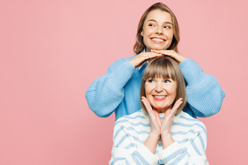 Elder parent mom 50s years old with young adult daughter two women together wear blue casual clothes stand behind mother hold hands on head isolated on plain light pink background. Family day concept. - obrazy, fototapety, plakaty
