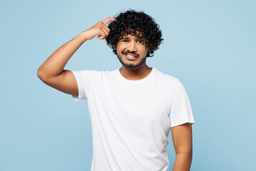 Young mistaken upset disappointed sad Indian man wear white t-shirt casual clothes look camera scratch hold head isolated on plain pastel light blue cyan background studio portrait. Lifestyle concept. - obrazy, fototapety, plakaty
