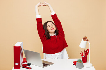 Young relaxed employee business woman she wear red sweater shirt sit work at office desk with pc...
