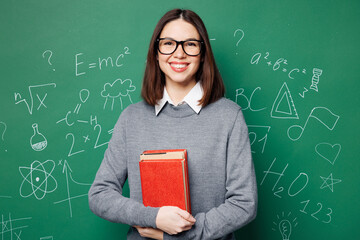 Young fun smiling smart teacher woman wear grey casual shirt glasses hold in hand book look camera isolated on green wall chalk blackboard background studio. Education in high school college concept.