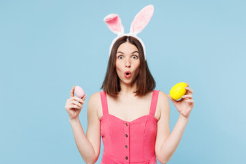 Young shocked surprised woman wear pink casual clothes rabbit bunny ears hold in hand painted eggs...