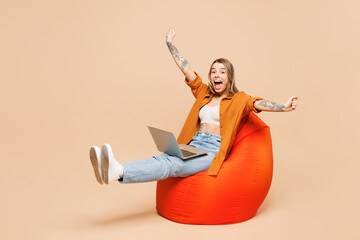 Full body young IT woman she wear orange shirt casual clothes hold use work on laptop pc computer do winner gesture isolated on plain pastel light beige background studio portrait. Lifestyle concept.