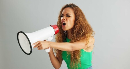 Angry woman, shouting and protest with megaphone for power, rights or equality on a gray studio...