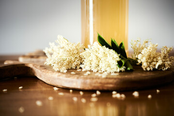 Bottle detail of homemade fresh elderflower cordial juice with small white elderflowers. Spring sweet drink or refreshing nonalcoholic elderberry flowers beverage on wooden board