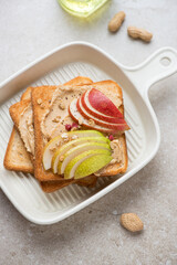 Beige serving tray with peanut butter and pear toasts, vertical shot on a beige stone background, elevated view