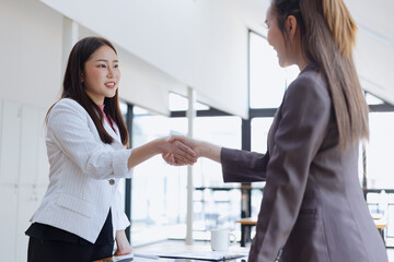 Businesswoman partnership handshake concept. Two young asian business professionals celebrating teamwork in an office, Colleague in meeting.