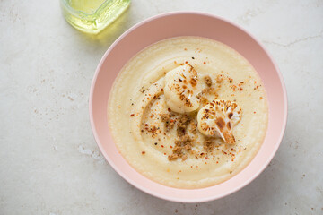 Roseate bowl with cream-soup made of roasted cauliflower, horizontal shot on a light-beige stone background, high angle view
