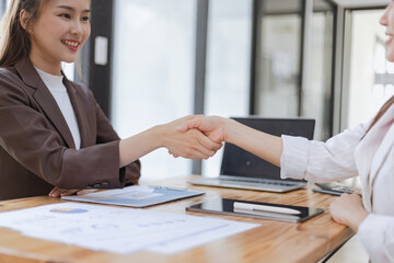 Businesswoman partnership handshake concept. Two young asian business professionals celebrating teamwork in an office, Colleague in meeting.