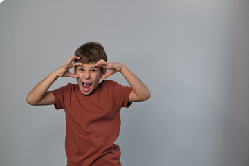 A boy in a rust-colored shirt makes a monster face, fingers pulling his eyes wide. This playful...