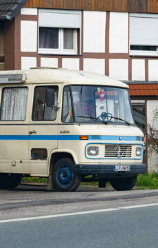Oldtimer Kleinbus Mercedes transporter O309 mit travel-box Reisemobil mit Vorh&auml;ngen parkend vor einem Fachwerkhaus