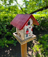 Obraz na płótnie Canvas A hand-painted birdhouse with a vibrant red roof and illustrations of birds, perched outdoors with a lush green background