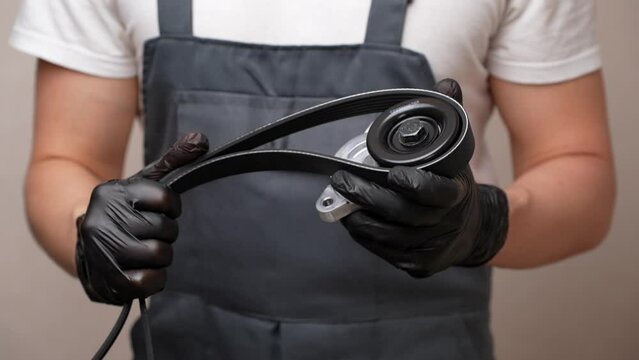 Auto parts salesman holds a tension pulley and a serpentine belt in his hands. Timely replacement of auto parts and vehicle maintenance. Sale of automotive products, provision of car repair services