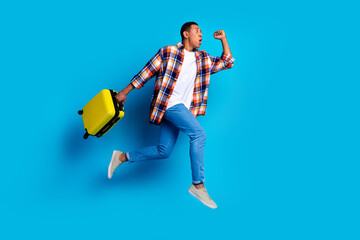 Full body portrait of nice young man suitcase jump run empty space wear shirt isolated on blue...