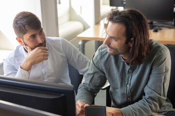 deux collègues, jeunes employés de bureau travaillent en équipe et discutent assis devant un ordinateur portable - 775757969