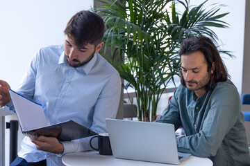 deux collègues, jeunes employés de bureau travaillent en équipe et discutent assis devant un ordinateur portable - 775758131