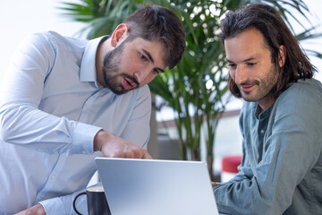 deux collègues, jeunes employés de bureau travaillent en équipe et discutent assis devant un ordinateur portable - 775758195