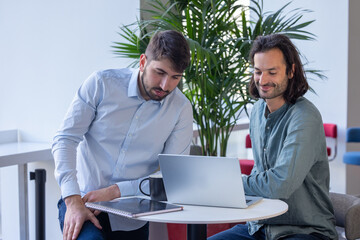 deux collègues, jeunes employés de bureau travaillent en équipe et discutent assis devant un ordinateur portable - 775758196