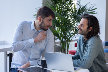 deux collègues, jeunes employés de bureau travaillent en équipe et discutent assis devant un ordinateur portable - 775758301