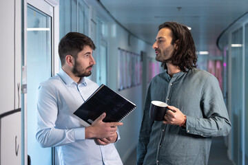 deux collègues discutent devant leur bureau dans les couloirs de leur entreprise pendant la pause café