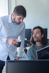 deux collègues, jeunes employés de bureau travaillent en équipe et discutent assis devant un ordinateur portable