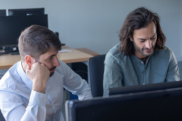 deux collègues, jeunes employés de bureau travaillent en équipe et discutent assis devant un ordinateur portable - obrazy, fototapety, plakaty