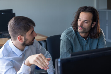 deux collègues, jeunes employés de bureau travaillent en équipe et discutent assis devant un ordinateur portable - 775759376