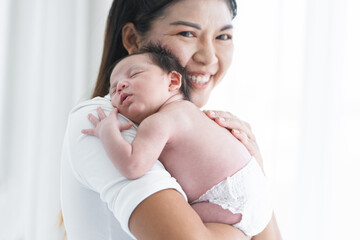 Mother carrying her newborn baby girl on shoulder at home. Cute 19 days Asian Australian infant...