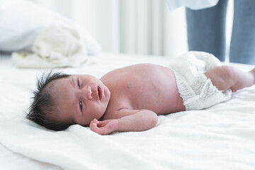 Portrait of beautiful newborn sleeping baby girl , lying on bed at home. Asian Australian infant 19 days old wear diaper with innocent sleepy face