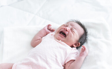 Newborn baby girl crying and screaming, lying on bed at home. Asian Australian infant 19 days old...