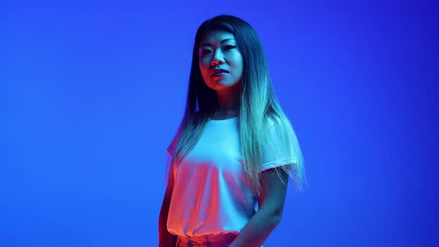 Confident, beautiful Asian woman, business lady posing looking at camera against blue gradient background in neon light. Concept of business, entrepreneurship, human emotions, self-expression.