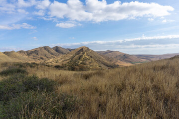 Landscape view of mountains. Dry orange grass. Bright blue sly with clouds. Desert region of...